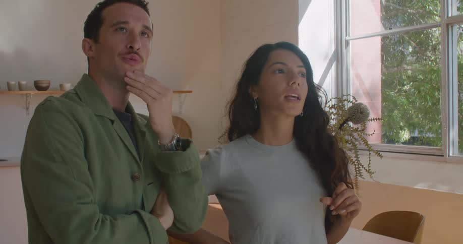 A man and woman stand in a kitchen while looking around and discussing their ideas