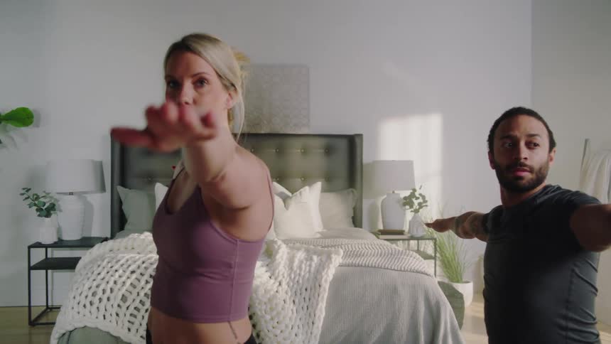 Man and woman move through yoga poses in their bedroom