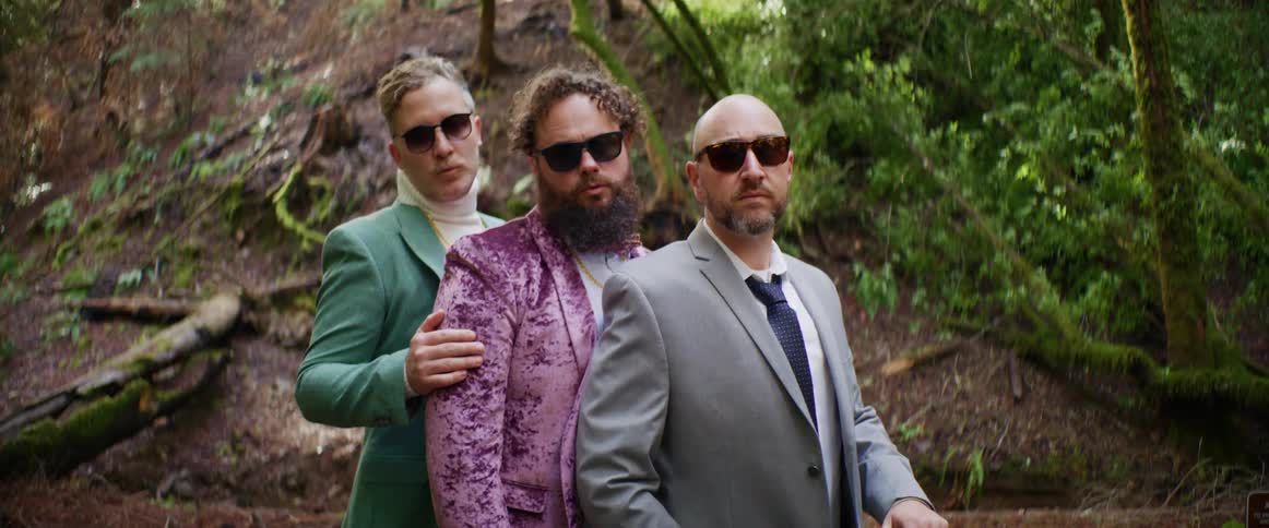 Three men pose together by the hill