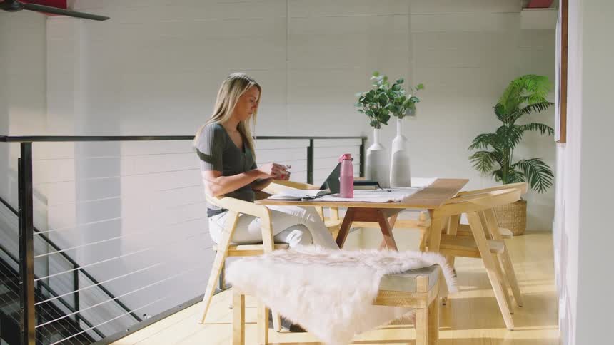 Blonde woman with green shirt white pants sits at table wearing wireless earphones using tablet