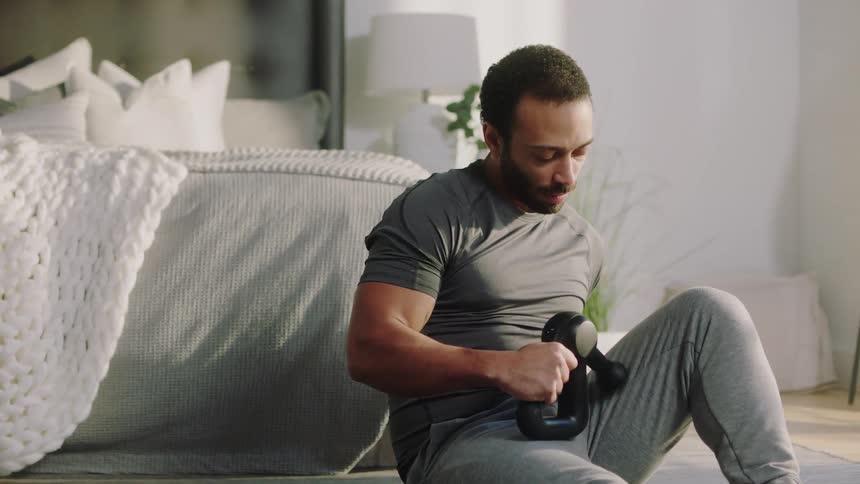 Man sits on floor near bed using hand held massage machine
