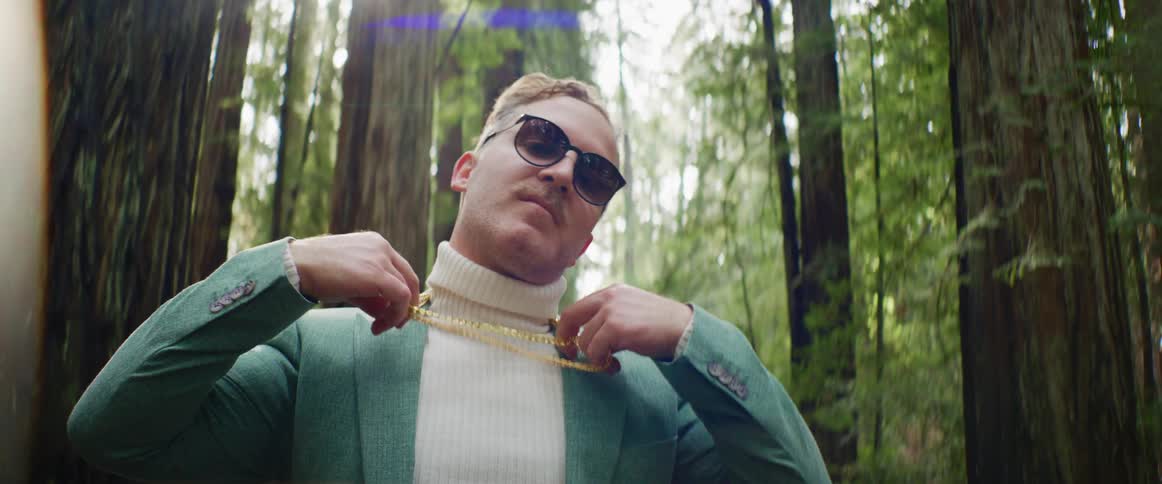 A man in gold chains and a turtleneck sweater posing