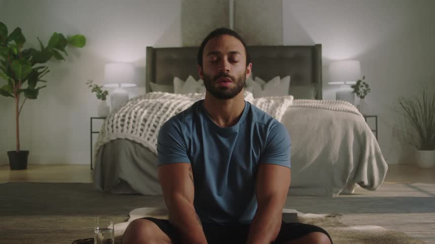 A man sitting on the floor of his bedroom with legs crossed and eyes closed taking deep cleansing breaths