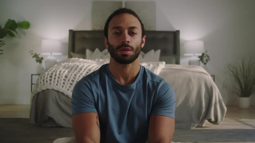 A man is taking deep breaths on the floor of a bedroom