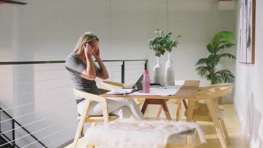 Woman sitting at table with computer puts on earphones then participates in video conference
