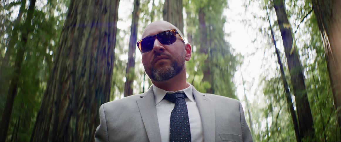 A man in a suit is posing for a camera in a forest