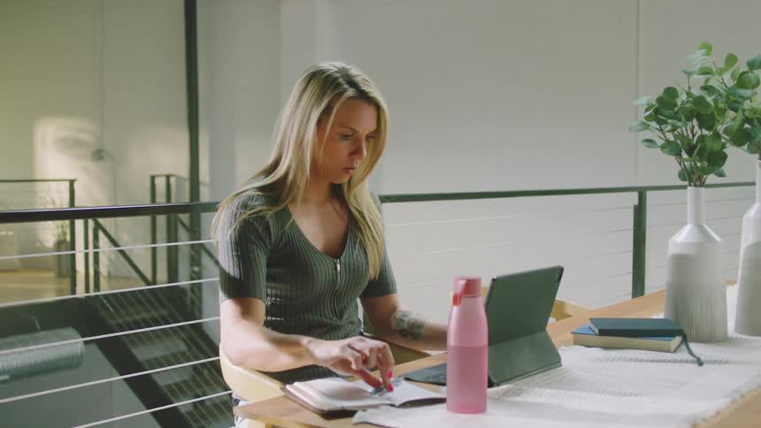 A woman drinks water and takes notes in her notebook