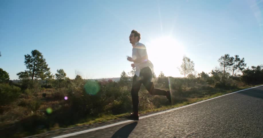 A man jogs on the shoulder of a sloped road