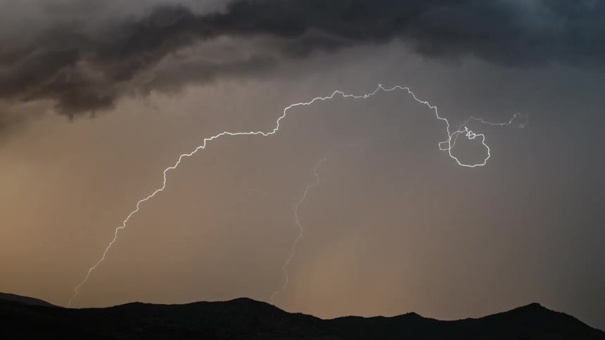 Lightning flashes across the sky in jagged lines from dark gray clouds