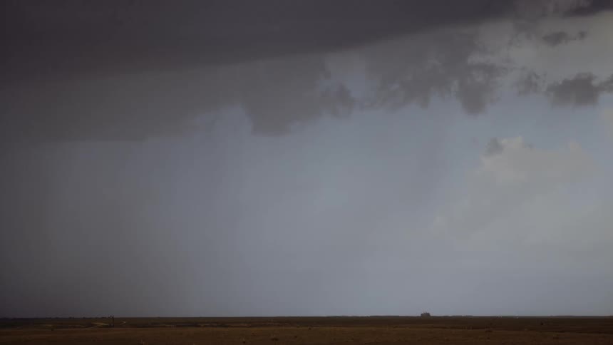 Lightning strikes down from dark gray storm clouds with blue sky still visible