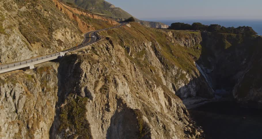 Aerial view of cars driving along side a mountain is displayed