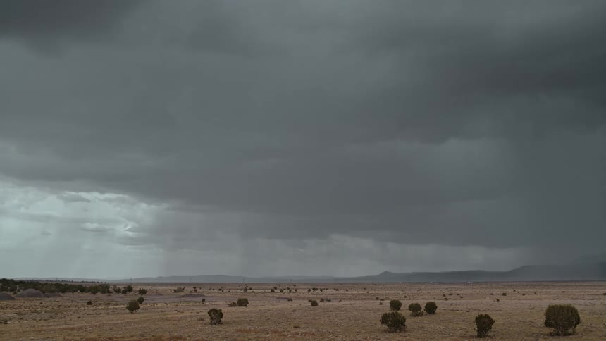 Lightning flashes in the stormy sky over the desert as mountains sit in the distance
