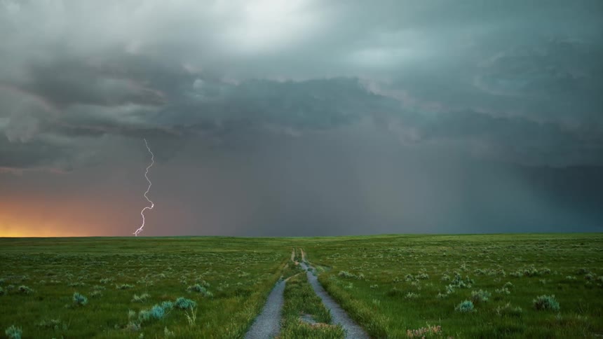 Its storming over a grassy landscape at dusk