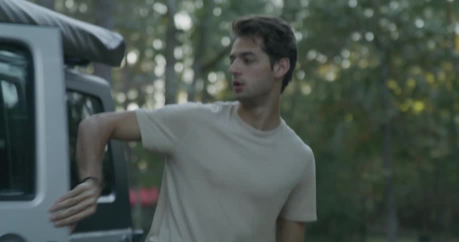 Man exits a vehicle and walks off with a woman in a clearing in the forest
