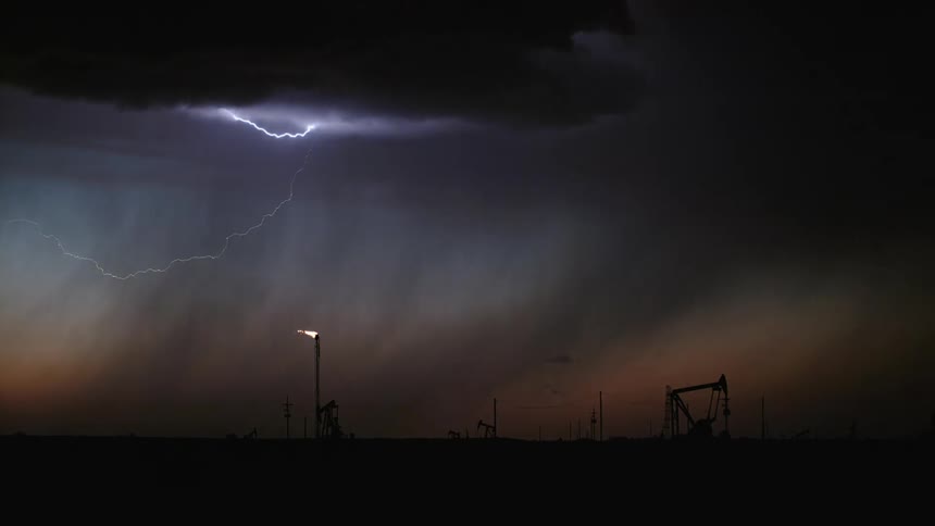 A landscape view of dark storm clouds and lightning flashing over an oil rig