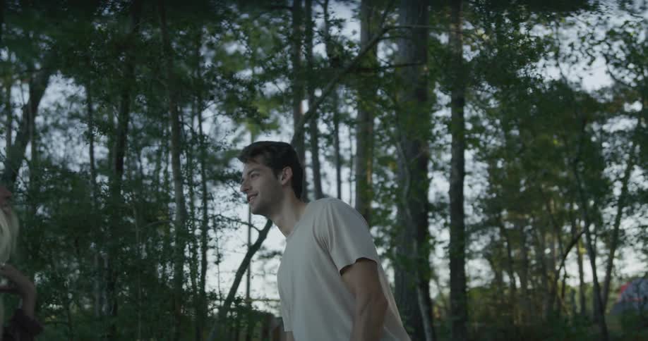 A group of young men and women walk through the forest holding things