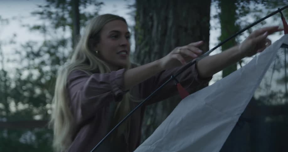 A woman is setting up a tent in a wooded area