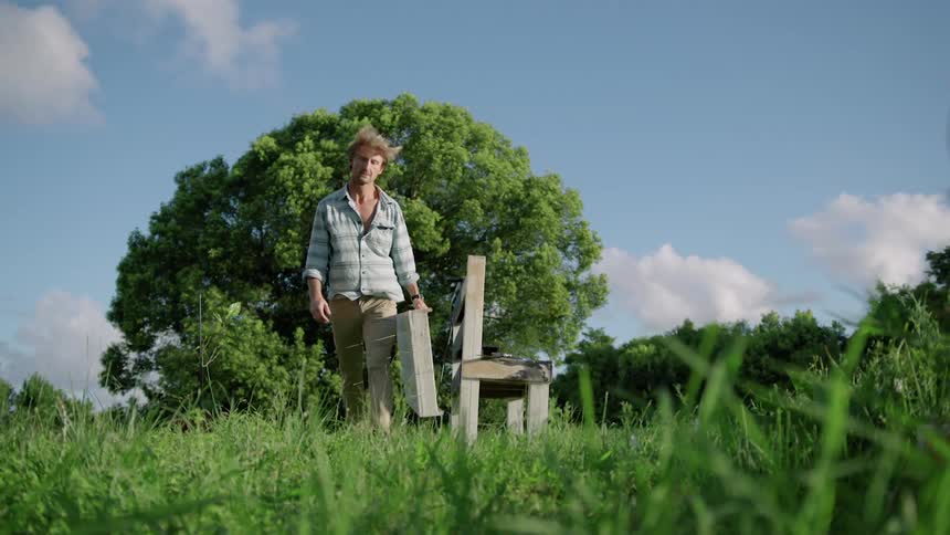 A man pics up a wooden object resting against another in a field