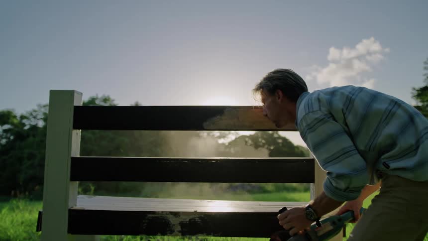 A man sands a wooden object in a field
