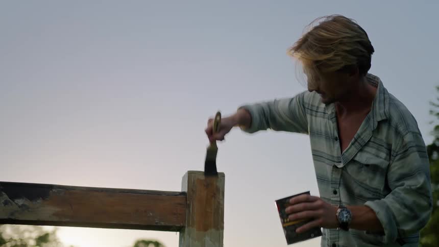 A man is staining a wooden object with a brush outdoors