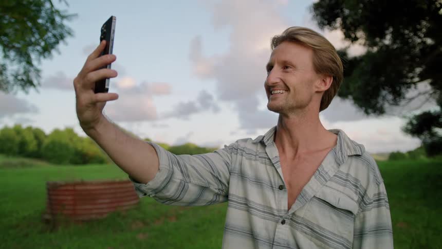 A man smiling and waving on an outdoor video call in summer