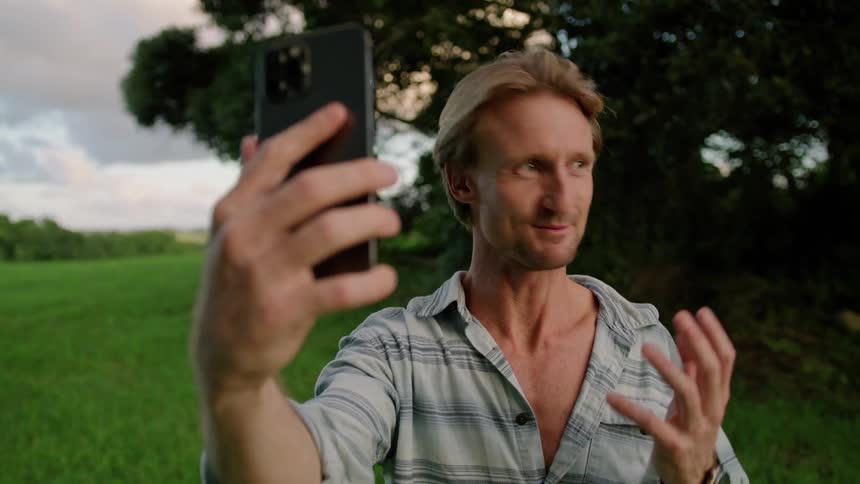 A man smiling and waving while on a video call outside on a summer day