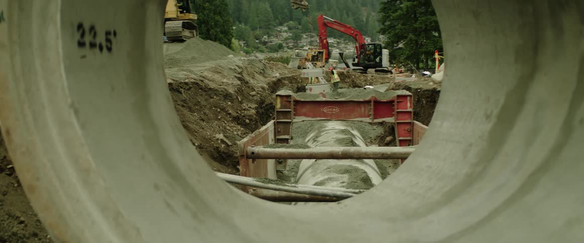 Workers placing down underground concrete pipes on a construction site close to a forest