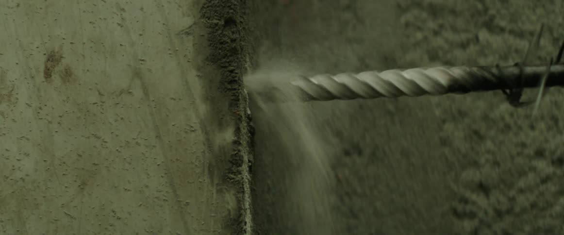 A drill bit drilling into a cement wall causing dust to fly