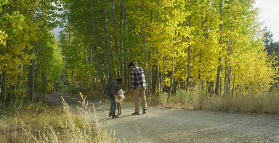 Mom picks up her little girl and then continues to walk the wooded trail with her husband