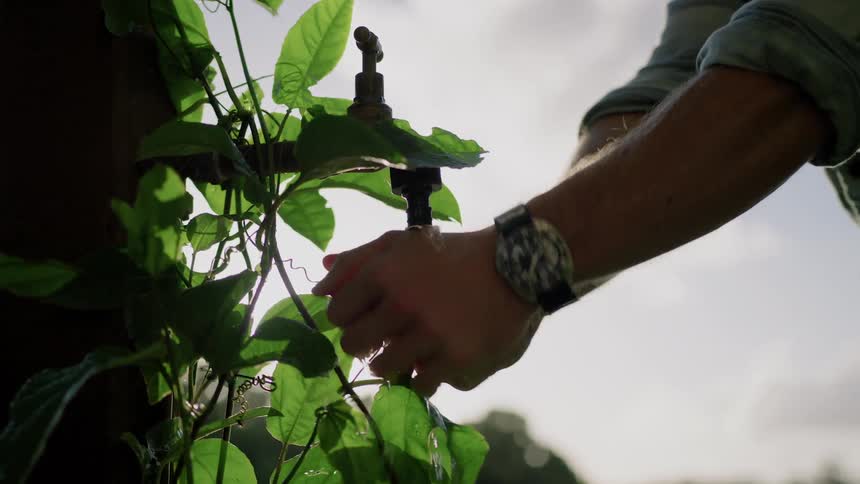 A man turns on an outdoor faucet to wash his hands in the garden