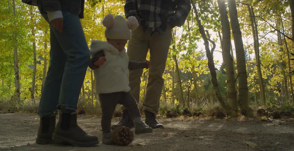 Baby girl kicking a pinecone on a trail in the forest as parents watch