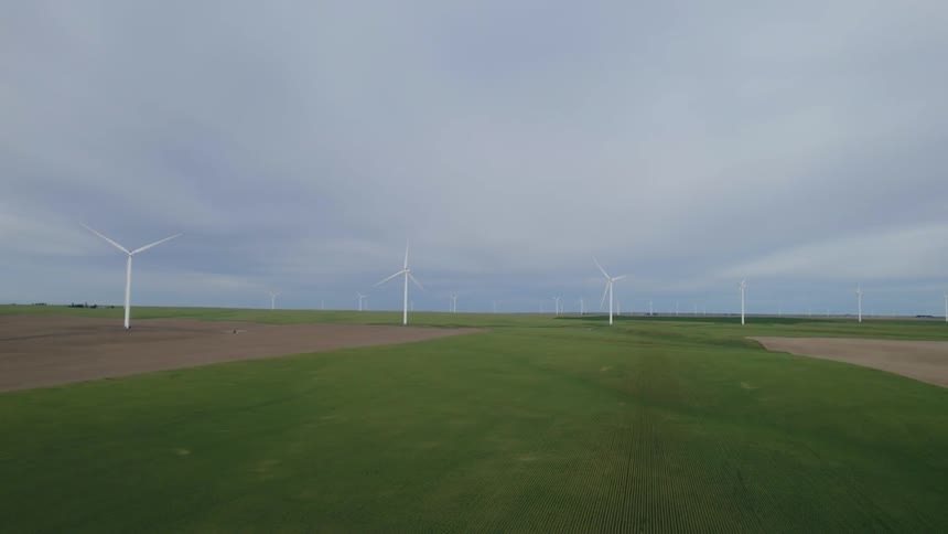 Wind turbines stand in green grass with patches of soil on a cloudy day