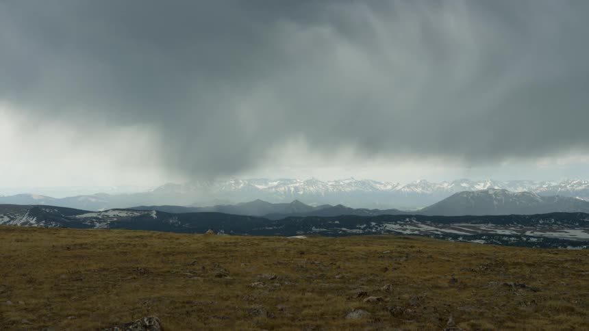 Dark clouds move over a field and snow capped mountains