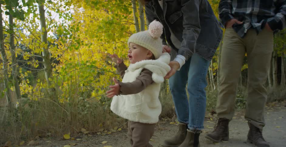 Parents supervising a toddler walking on a trail through the forest at morning