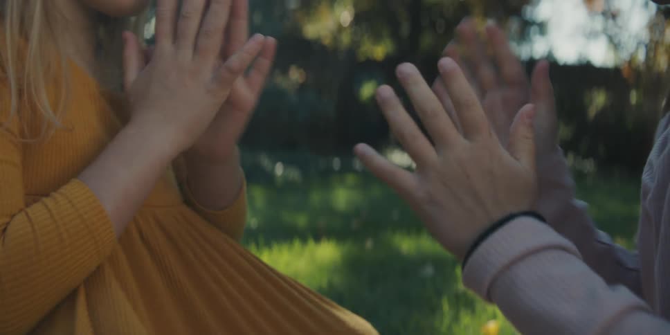 Two girls sit in the grass and play patty cake