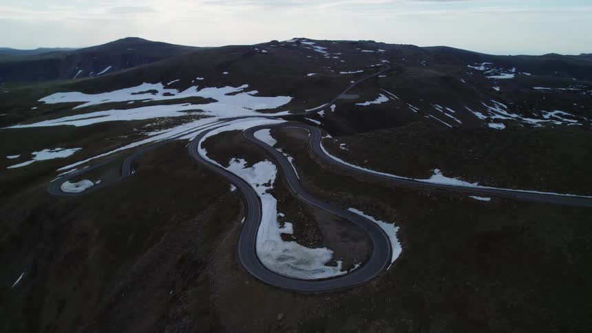 Aerial view of biker riding motorcycle on winding road on snowy hill