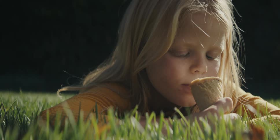 A girl lies in the grass and licks an ice cream cone