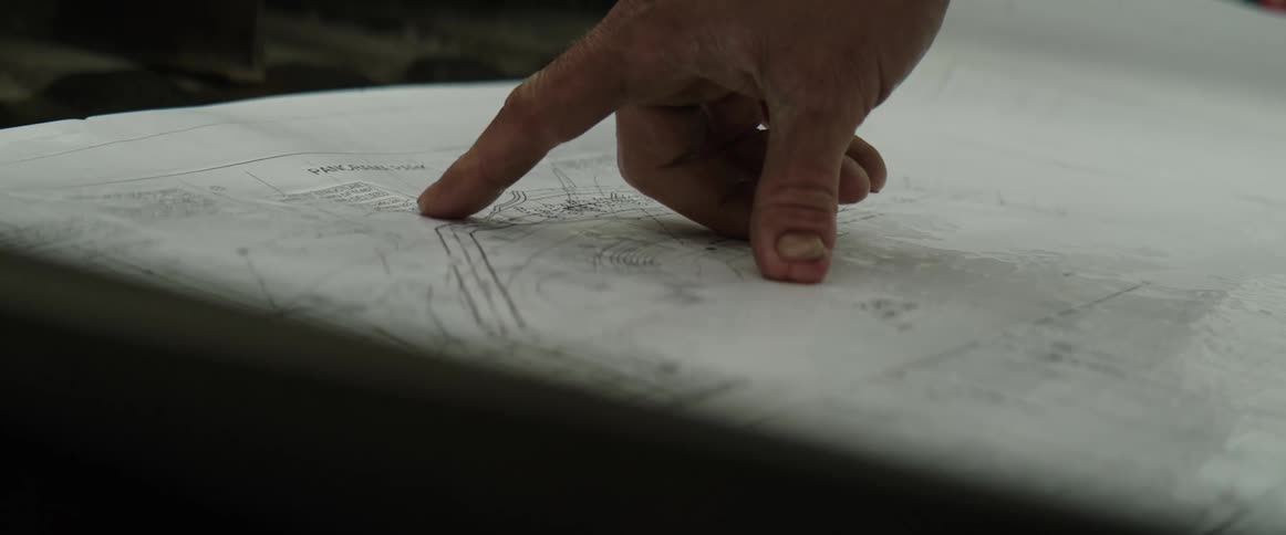 A persons hand is pointing to an area on blueprints sitting on a table