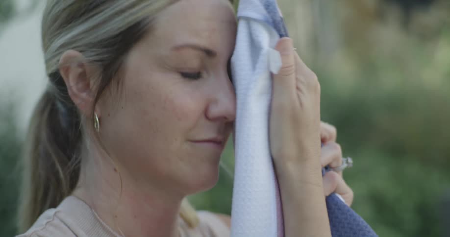 Middle aged blonde woman with ponytail dries sweat using towel