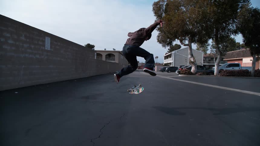 Man jumps in the air as he rides a skateboard on the street near the trees