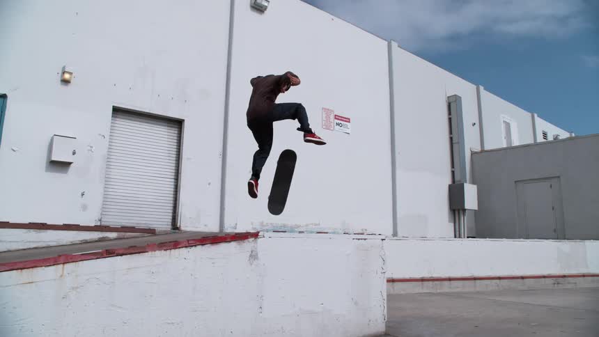 Skateboarder jumping off a loading dock ramp behind a white building