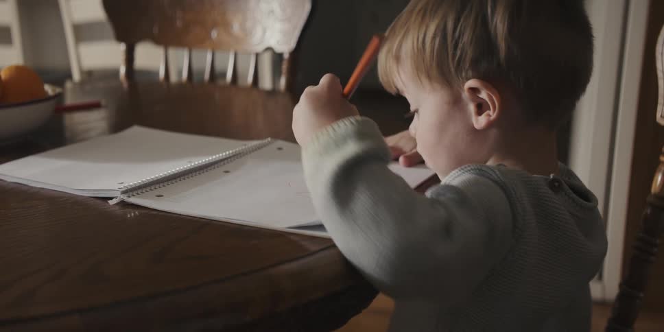 A young boy uses a pencil to write in a notebook at a table