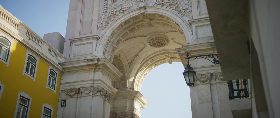 Clock on the top of an arched building with pedestrians walking under the arch
