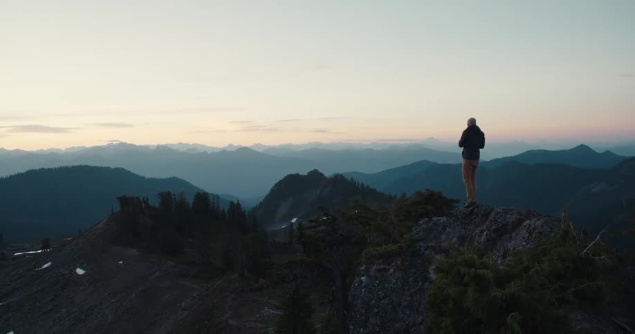 A man standing on a mountain ledge takes photos