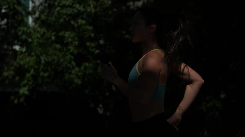Woman with sports bra black leggings and white running shoes jogs on tree tunnel road in the street