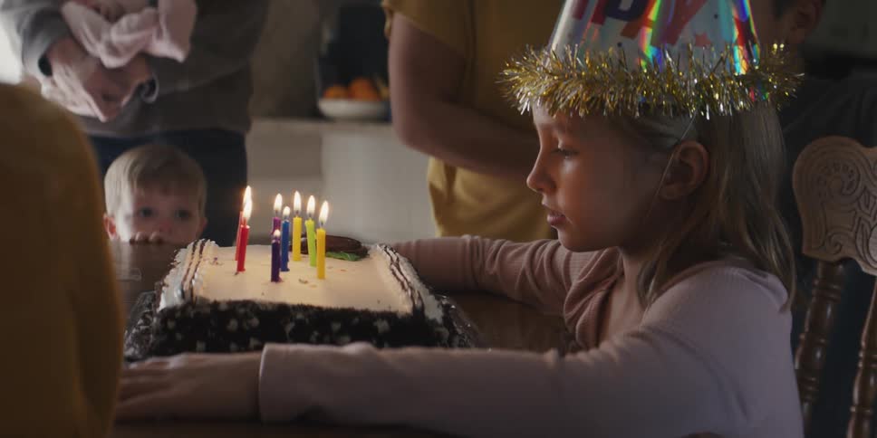 A young girl sitting in front of a birthday cake with lit candles at a birthday party