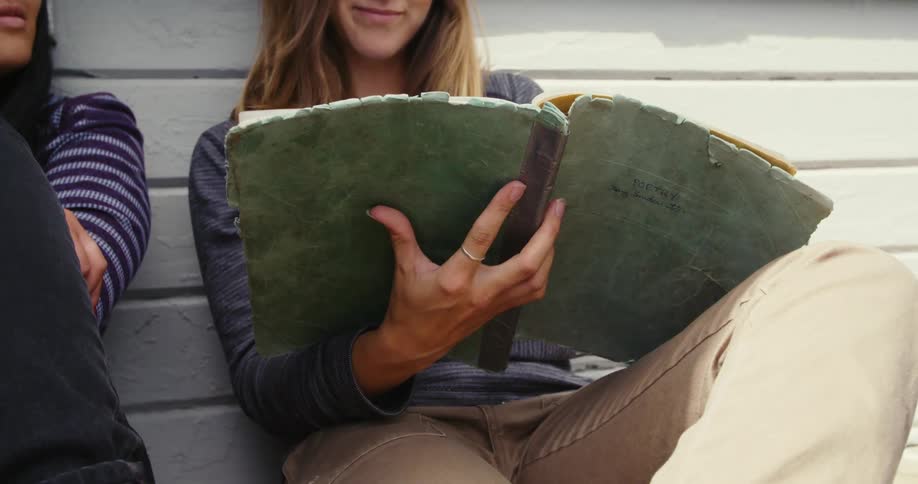 Two friends are sitting outdoors and reading a book