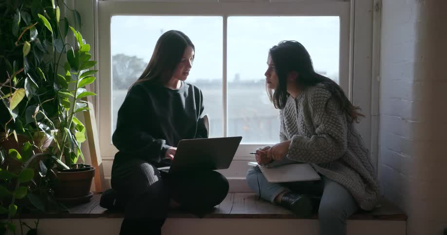 Two women work next to a window