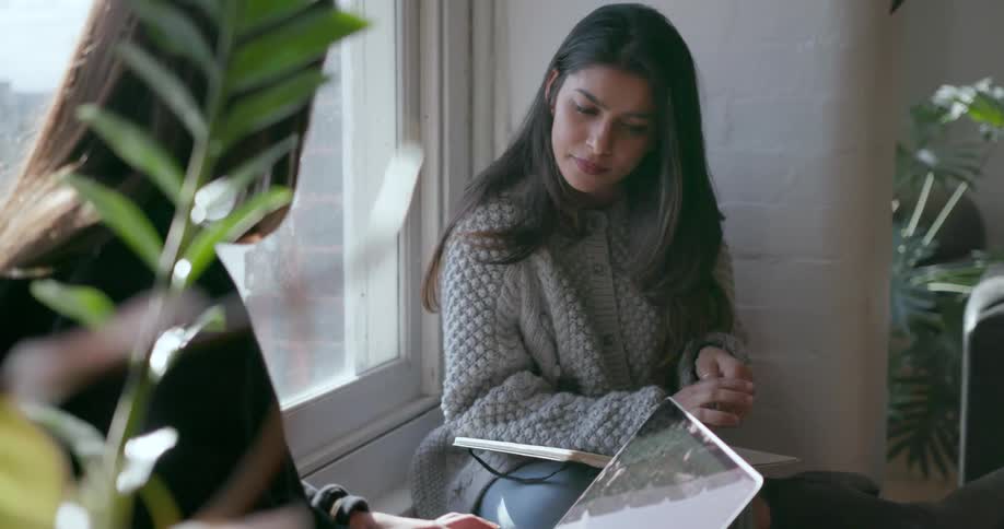 Two women have a conversation at a window sill
