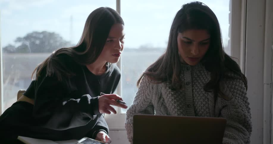 Two girls study next to a window